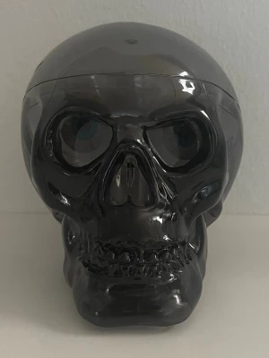 Svart dödskalle maskeradaccessoar - Cool dödskalle i svart plast, perfekt som dekoration eller accessoar till maskerad och cosplay. Skallen har tydliga detaljer och en blank finish som ger ett mystiskt och edgy intryck. Passar till halloween eller temafest.