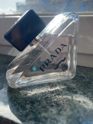 Helt ny Prada Paradoxe Virtual Flower parfym - Prada Paradoxe Virtual Flower Eau de Parfum i en unik, trekantig glasflaska med svart fyrkantigt lock. Flaskan är transparent och elegant med tydlig logga och text i svart. Doften är modern och exklusiv, perfekt för dig som gillar lyxiga parfymer.