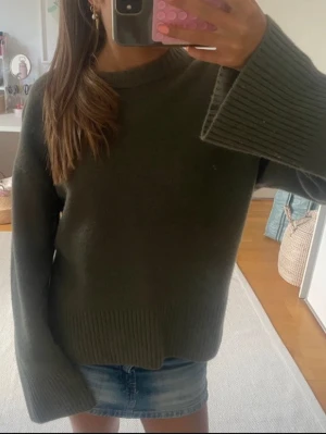 Olivgrön stickad tröja - Säljer denna supersnygga mörkgröna stickade tröjan i mjukt och lyxigt material från Arket. Den har slits på sidan och en oversized modell. 25% kashmir. Tröjan har en avslappnad, oversized passform och rund halsringning. 💚💚