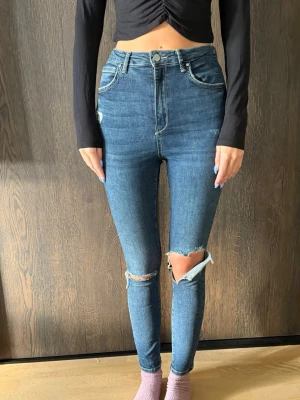 Gina tricot jeans size EU 38 - Säljer ett par blå skinny jeans med hög midja och slitningar vid knäna. Jeansen har klassiska fickor och är i stretchigt denimtyg som sitter tight hela vägen ner. 