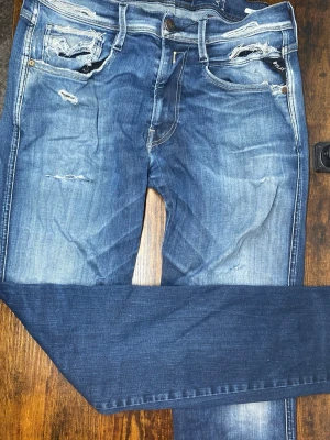 Replay Abbas’s - Säljer ett par blå replay jeans med slitningar och ljusa tvättade partier. Jeansen har klassisk femficksmodell och smal passform hela vägen ner. Perfekta för en avslappnad och trendig look.