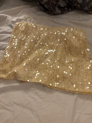 Gul paljettkjol från Gina Tricot - Snygg kort gul kjol från Gina Tricot täckt med glittriga paljetter. Kjolen har en rak passform och är perfekt för dig som vill sticka ut med lite extra bling. Materialet känns mjukt och bekvämt mot huden.