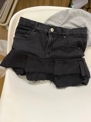 Svarta volangshorts från ONLY - Säljer ett par svarta shorts från ONLY med volangdetalj nedtill och råa kanter. Klassisk femficksmodell med knapp och dragkedja framtill. Perfekta för dig som vill ha en trendig och edgy look.