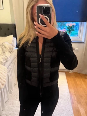 Svart cardiganjacka från Moncler - Snygg svart cardiganjacka från Moncler med quiltad front och två fickor på varje sida. Jackan har dragkedja framtill, ribbade muddar och Moncler-logga på ärmen. Perfekt för lager-på-lager och ger en sportig men stilren look.