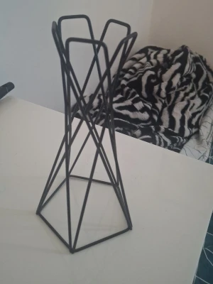 Svart geometrisk metallställ - Säljer ett svart ställ i metall med geometrisk design. Perfekt som dekoration eller förvaring av exempelvis flaskor eller rullar. Stället har en öppen, luftig form och står stadigt på sex ben.