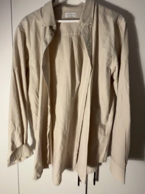 Beige skjorta från These Glory Days - Säljer en stilren beige skjorta från These Glory Days i storlek XL. Skjortan har klassisk krage, långa ärmar och knappar framtill. Perfekt att matcha med jeans eller chinos för en clean look.