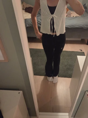 Vit croppad linnetopp med knyt - Säljer en söt vit ärmlös linnetopp med knyt framtill. Toppen har en v-ringad hals och är croppad i modellen, perfekt att styla över ett linne eller t-shirt. Enkel och stilren design som passar till mycket.Det finns slitages på ändarna av knytbanden och några trådar har lossnat, vilket syns på bilderna. Därför säljs den billigare❤️.        Det är storlek XS