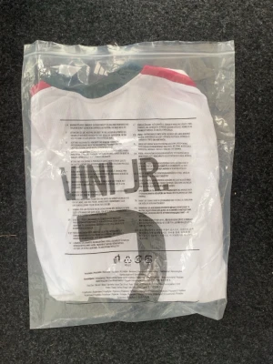 Real Madrid hemmaställ 26/27 - Snygg vit Real Madrid matchtröja från Adidas med Vini Jr. och nummer 7 på ryggen. Tröjan har mörkgröna detaljer, rosa ränder på axlarna och klubbmärke på bröstet. Tillverkad i lätt och ventilerande material, perfekt för fotbollsträning eller match. HELT NY, ALDRIG ANVÄND!
