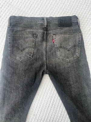 Svarta slim fit jeans från Levi's - Snygga svarta slim fit jeans från Levi's med klassisk femficksdesign och diskret slitning framtill. Jeansen har raka ben och är tillverkade i ett mjukt denimtyg med stretch för extra komfort. Perfekta för en trendig och avslappnad stil. W33 L32