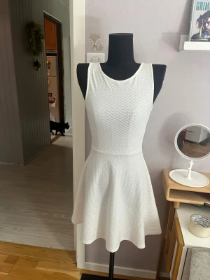 👗 Vit strukturerad skaterklänning (H&M Divided, stl 34) - Säljer en jättesöt, vit ärmlös klänning från H&M Divided i storlek 34 (XS). Klänningen har en figurnära överdel med rund halsringning och en jättefin utsvängd skater-kjol. Tyget har en superfin, lätt bikakestruktur/våfflad textur som gör att den faller väldigt fint.Perfekt som sommarklänning, till midsommar, studentfester eller andra festliga tillfällen! ✨