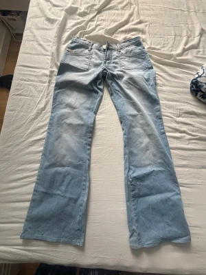 Ljusblå bootcut jeans med fickdetaljer - Snygga ljusblå jeans med bootcut passform och coola fickdetaljer bak. Jeansen har klassisk femficksdesign och är tillverkade i denim. Perfekta för en avslappnad och trendig look.