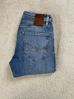 Blå jeans från Jack & Jones - Snygga blå jeans från Jack & Jones med klassisk femficksdesign och slitningar framtill. Jeansen har normal midja, raka ben och är gjorda i ett mjukt denimtyg. Perfekta för en avslappnad och trendig look.