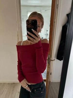Röd offshoulder ribbad topp - Trendig röd offshoulder topp med lång ärm och ribbad struktur. Sitter tight och har en bred kant upptill som ger en snygg siluett. Perfekt för dig som vill ha en stilren men ändå iögonfallande look.