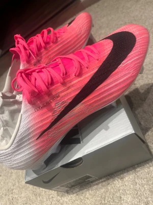 Nike Mercurial rosa fotbollsskor - Säljer ett par Nike Mercurial fotbollsskor i en grymt snygg rosa färg med svart swoosh. Skorna har en gradient från vitt till rosa, snörning och avancerad yttersula med Air Zoom-teknologi för maxad speed. Perfekta för dig som vill sticka ut på planen.