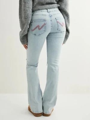 Ljusblå bootcut jeans med slitningar - Säljer ett par ljusblå bootcut jeans med slitningar över knäna och broderade detaljer i rött på bakfickorna. Jeansen har klassisk femficksdesign och är tillverkade i denim med en avslappnad passform. Perfekta för en trendig och avslappnad look.