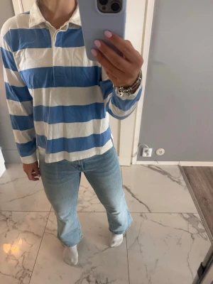 Blå/vit randig rugby tröja från Kappahl  - Blå/vit randig tröja med krage från Kappahl. Kragen/urringningen kan justeras med knappar.  Strl S, används ej längre. Nypris 399kr, men säljs ej längre. Meddela för frågor.