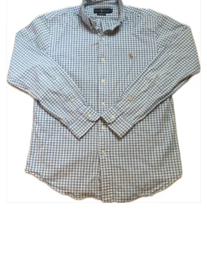 Blårutig skjorta från Ralph Lauren - Säljer en blårutig skjorta från Ralph Lauren i slim fit stretch oxford. Skjortan har klassisk krage, knappar framtill och lång ärm. Ikoniska broderade loggan på bröstet. Perfekt för dig som gillar stilrena och tidlösa plagg.