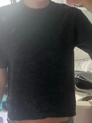 Svart croppad stickad topp - Mysig svart croppad stickad topp med korta ärmar och rund hals. Perfekt till jeans eller kjol för en enkel och stilren look.