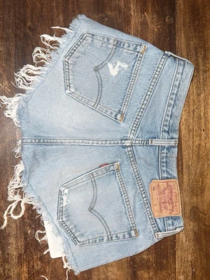 Levi’s 501 shorts - Säljer ett par ljusblå jeansshorts med fransiga benslut och slitna detaljer. Ca storlek 36, lappen är bortklippt. Du står för frakten 💕(de sitter ganska högt i midjan på mig som är 154 cm, borde vara midwaist på en lite längre)
