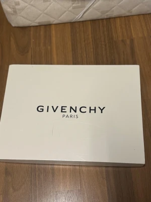 Givenchy zip pouch - Jaws collab - Vintage - Säljer en svart plånbok från Givenchy med ett coolt hajmotiv på framsidan. Plånboken är tillverkad i slätt läder och har Givenchy Paris-loggan i guld upptill. Perfekt accessoar för dig som vill sticka ut. Köpte 10 år sen aldrig använt