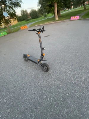 Svart elsparkcykel med orange detaljer - Säljer en svart elsparkcykel med orange detaljer. Den har breda däck, robust ram och handtag med display. Utrustad med fram- och bakljus samt reflexer för extra synlighet. Perfekt för att ta sig runt i stan på ett smidigt sätt.
