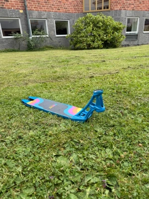 Ethic pandemonium v1 - Säljer ett blått sparkcykeldeck med färgglada vågmönster i rosa, gult och lila på ovansidan. Deckets material är metall och det har en robust konstruktion med öppningar framtill för styrstång. Perfekt för dig som vill bygga din egen trick-scooter.