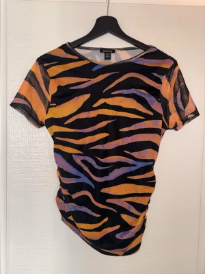Zebramönstrad mesh t-shirt Boohoo - Cool zebramönstrad t-shirt från Boohoo i meshmaterial. T-shirten har korta ärmar och färger i svart, orange och lila. Perfekt för dig som vill sticka ut med en trendig och färgstark look.