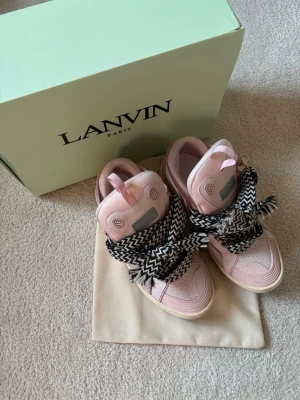 Lanvin rosa sneakers med mönstrade snören - Säljer ett par snygga rosa Lanvin sneakers med svartvita, zigzagmönstrade snören. Skorna har en chunky sula och detaljer i mocka och skinn. Perfekta för dig som vill sticka ut med en unik och trendig look.