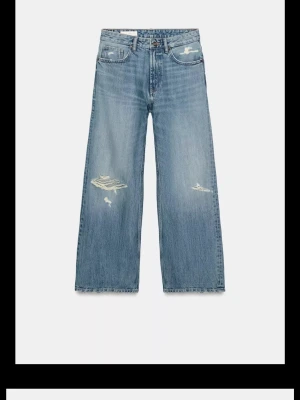Blåa wide leg jeans med slitningar - Säljer ett par blåa wide leg jeans med coola slitningar och råa kanter. Jeansen har hög midja, fem fickor och en avslappnad passform. Perfekta för en trendig och avslappnad stil. Materialet är klassisk denim i bomull. Dom är uppklippt några cm, klippta vid slitningarna längst ner så det ser naturligt ut