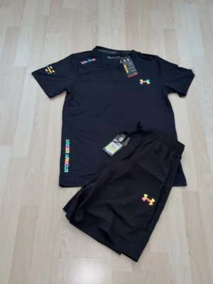 Svart träningsset från Under Armour - Säljer ett svart träningsset från Under Armour med t-shirt och shorts. Setet har färgglada loggor och detaljer, samt elastisk midja på shortsen. Perfekt för gymmet eller löpning. Materialet är lätt och andas bra.