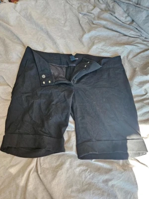 Svarta shorts från H&M - Snygga svarta shorts från H&M med uppvikta benslut och klassisk dragkedja samt knappstängning. Perfekta för varma dagar och enkla att matcha med olika stilar. Gjorda i ett mjukt och bekvämt material.