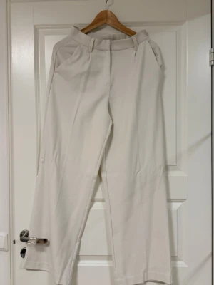 Vida vita kostymbyxor - Snygga kostymbyxor i vitt med hög midja och vida ben. Byxorna har bälteshällor, pressveck och fickor fram samt en dekorficka bak. Perfekta för en clean och stilren look. Materialet ser ut att vara en mjuk och lite tjockare väv. De är använda endast en gång men de var för långa för mig därför är de lite smutsiga nerifrån. Jag har inte tvättat de så jag tror om man tvättar de så kan smutset försvinna. Jag säljer de billigt för någon som behöver dom:)