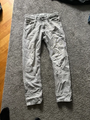 Ljusgrå raka jeans - Säljer ett par ljusgrå jeans med rak passform och klassisk femficksdesign. Jeansen har bälteshällor och knappgylf. Materialet är denim i bomull och färgen är snyggt tvättad ljusgrå. Perfekta för en avslappnad och trendig stil.