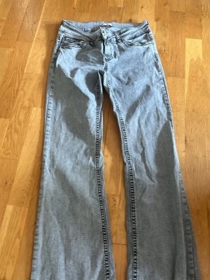 Ljusgrå bootcut jeans - Snygga ljusgrå jeans med bootcut passform och klassisk femficksdesign. Jeansen har en vågig detaljsöm på bakfickan och är tillverkade i denim. Perfekta för dig som gillar en avslappnad men trendig stil.
