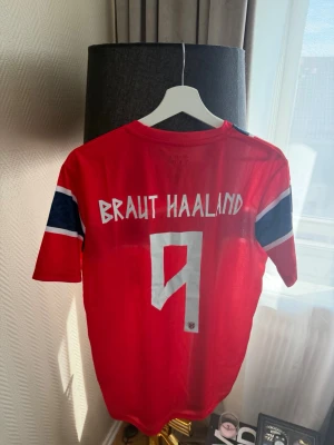 Norge fotbollströja Haaland stl M-L - Röd fotbollströja med norska flaggan över bröstet och ärmarna. Nummer 9 och texten 'Braut Haaland' på ryggen. Kortärmad modell med rund hals och klubbmärke på bröstet.  Storlek L men mycket mer lik en storlek M i passform