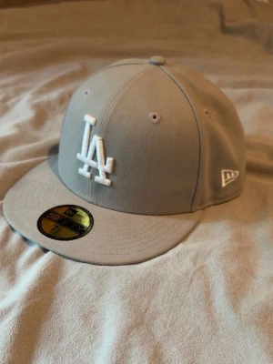 59 fifty keps grå - Snygg grå keps från New Era med LA-logga broderad framtill i vitt. Klassisk flat brim och strukturerad passform. Kepsen har New Era-logga på sidan och MLB-märke bak. Perfekt för dig som gillar streetwear och sportig stil.