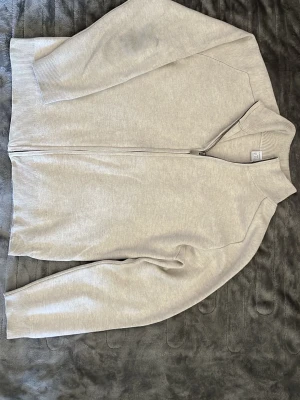 Beige ziptröja från Lindex - Snygg beige ziptröja från Lindex med hög krage och hel dragkedja framtill. Tröjan har ribbade muddar vid ärmslut och nederkant, perfekt för en avslappnad och stilren look. Passar dig som gillar enkel och clean stil.