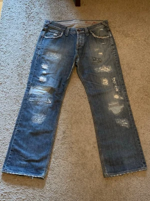Blå slitna jeans med raka ben - Om undras om mått så kan ja skicka! Säljer ett par blå jeans med raka ben och tydliga slitningar och lagningar på både fram- och baksida. Jeansen har klassisk femficksmodell, bälteshällor och dragkedjegylf. Perfekta för en avslappnad och trendig streetstil.