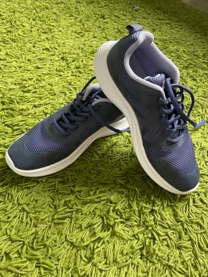 Blå mesh sneakers med vita sulor - Snygga sneakers i marinblått med ovandel i mesh och syntetmaterial. Skorna har vita, räfflade sulor och matchande blå skosnören. Låg modell som passar perfekt till jeans eller träningskläder. Lätta och bekväma för en aktiv vardag.