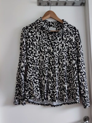 Svartvit mönstrad skjorta Andcowoman - Säljer en svartvit skjorta från Andcowoman i storlek 2XL. Skjortan har ett unikt abstrakt mönster, klassisk krage och långa ärmar. Perfekt för dig som gillar statement-plagg och vill sticka ut lite extra.