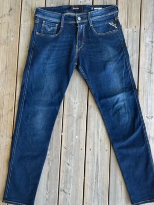 Mörkblå jeans från Replay - Säljer ett par mörkblå jeans från Replay i modellen Anbass. Jeansen har klassisk femficksdesign, raka ben och snygga slitningar. Materialet är mjukt denim med kontrastsömmar och knappgylf. Perfekta för dig som gillar en tidlös och stilren look.