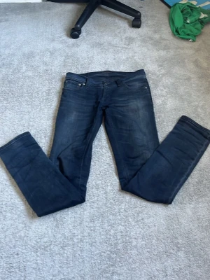 Mörkblå jeans från Nudie Jeans - Säljer ett par mörkblå jeans från Nudie Jeans i storlek W30 L34. Klassisk femficksmodell med smal passform och snygga slitningar på låren. Jeansen är tillverkade i mjukt denimtyg och har en stilren look som passar till det mesta.