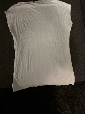 Vit ärmlös t-shirt i bomull - Säljer en enkel och stilren vit t-shirt utan ärmar. T-shirten har en rak passform och är tillverkad i mjuk bomull, perfekt för en avslappnad look. Passar till det mesta och är ett måste i garderoben.