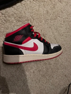 Svart, vit och röd sneaker - Sneaker i svart, vitt och rött med klassisk design och röd swoosh på sidan. Skon har röda skosnören och detaljer samt en vit mellansula och röd yttersula. Tillverkad i läder med tydliga paneler och logga på sidan.