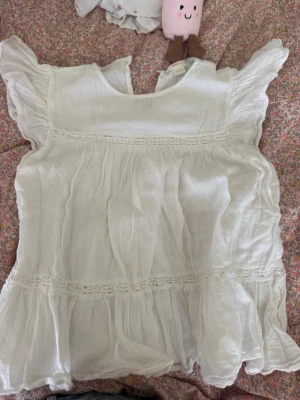 Vit blus med volang från Gina Tricot - Supersöt vit blus från Gina Tricot med volangdetaljer och spetsinslag. Blusen har korta, rynkade ärmar och en luftig, flowy passform. Perfekt till sommaren och lätt att matcha med jeans eller kjol.