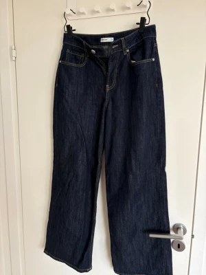 Mörkblå wide leg jeans Gina Tricot - Snygga mörkblå jeans från Gina Tricot med breda ben och hög midja. Klassisk femficksmodell med kontrastsömmar och robust denimkänsla. Perfekta för en trendig och avslappnad look.