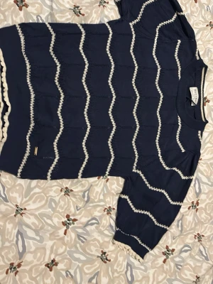 Blå tröja Holly & Whyte Lindex S - Mysig blå tröja från Holly & Whyte by Lindex i storlek S. Tröjan har vita vågiga ränder och ribbade muddar vid hals, ärmslut och nederkant. Materialet känns mjukt och lätt, perfekt för lager på lager. Snygg detalj med liten metallbricka vid nederkanten.