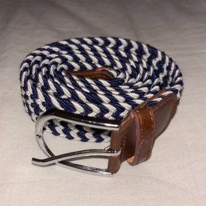 Trendigt flätat bälte! - Snyggt blå/vit randigt bälte med bruna skinnändar och ett silverspänne. Unna dig ett flätat bälte för att ge en extra touch till din outfit.