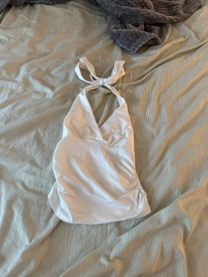 Vit halterneck linnetopp - Säljer en vit halterneck linnetopp med knyt i nacken och v-ringad front. Toppen är ärmlös och har en mjuk, lätt stretchig känsla. Perfekt för dig som vill ha en enkel men snygg topp