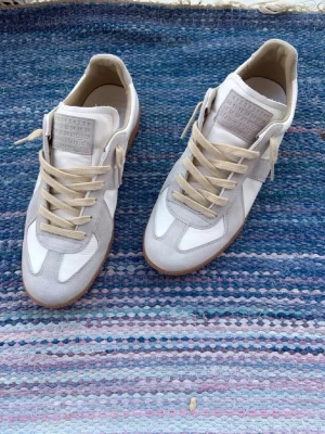 Maison margiela - Stilrena sneakers i vitt och ljusgrått från Maison Margiela. Skorna har beige snören, ovandel i mocka och läder samt klassisk gummisula. Perfekt för dig som gillar minimalistisk och clean stil.